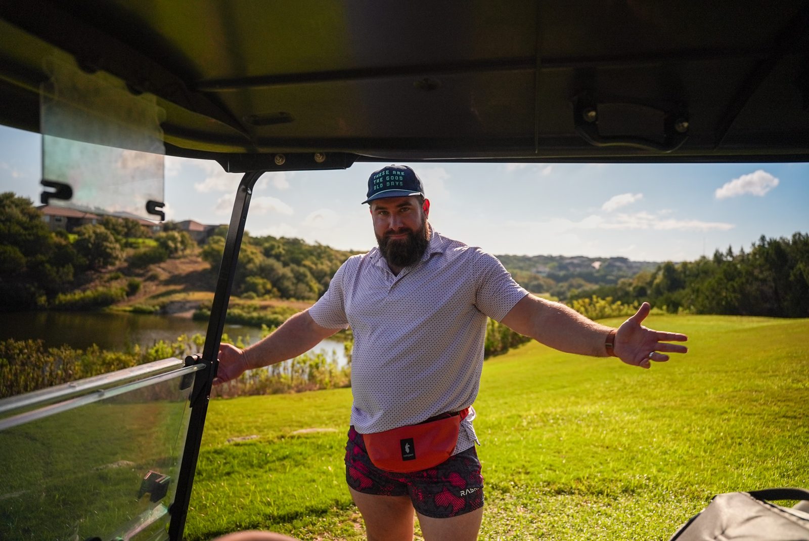 A golfer in a golf cart with his arms spread wide, Crystal Falls fairway behind him