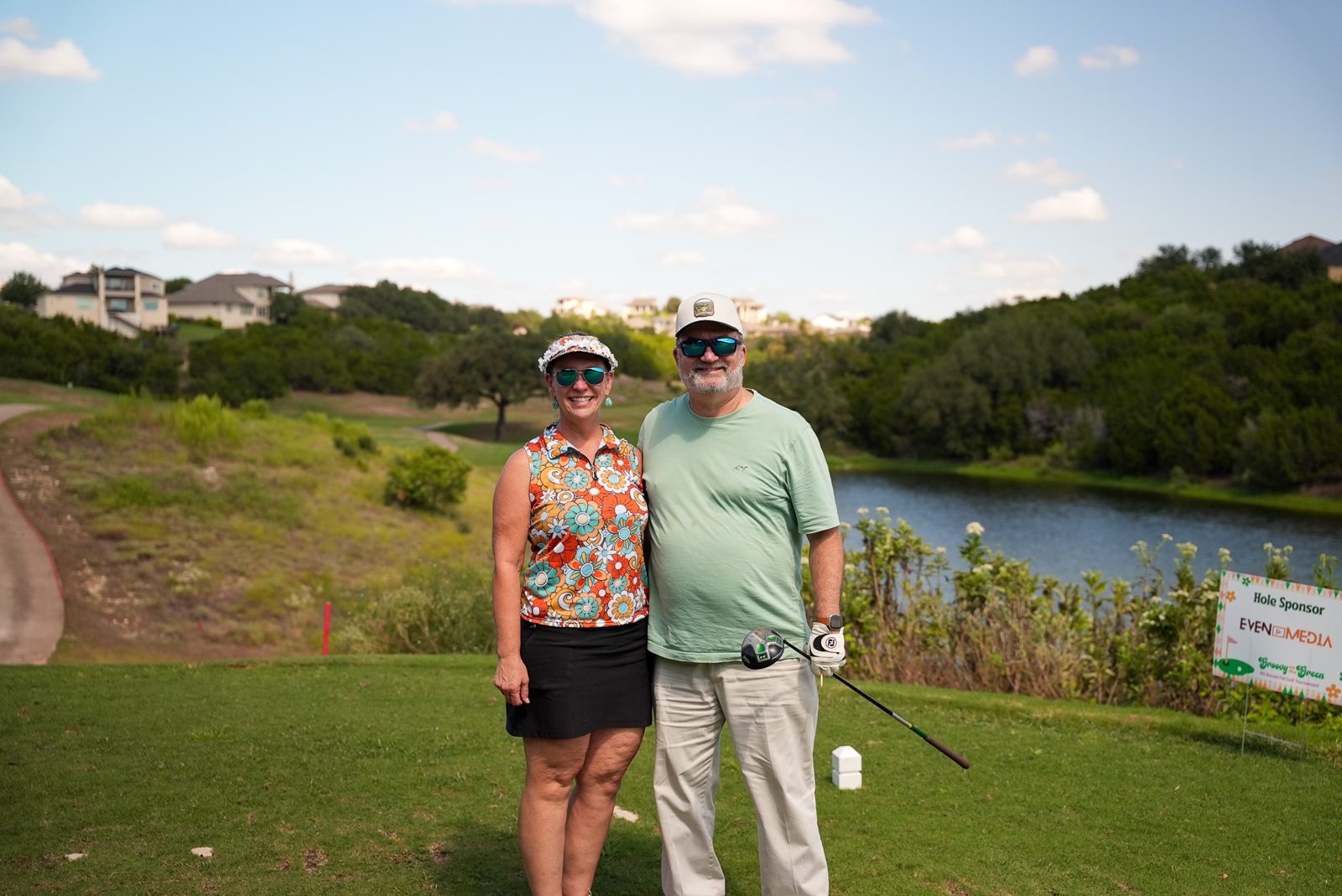 A couple poses on the tee at Hole 4 with the EVEN Media hole sponsor sign behind them