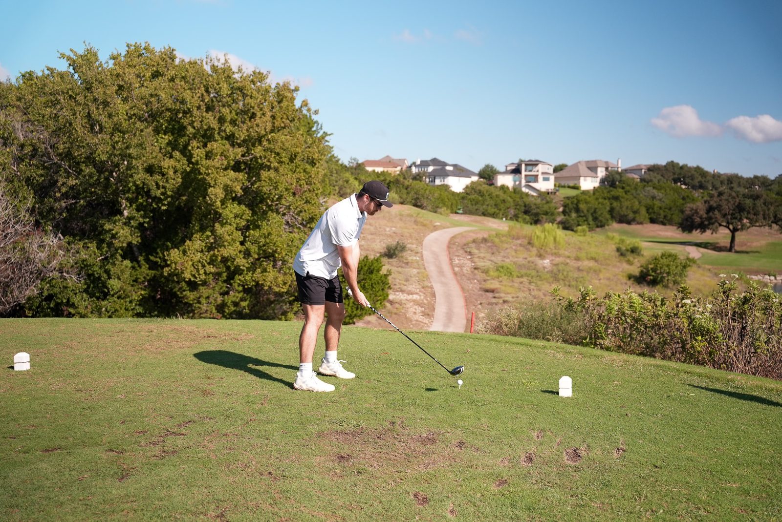 A golfer mid swing on the Hole 4 tee with the Crystal Falls fairway and houses in the distance